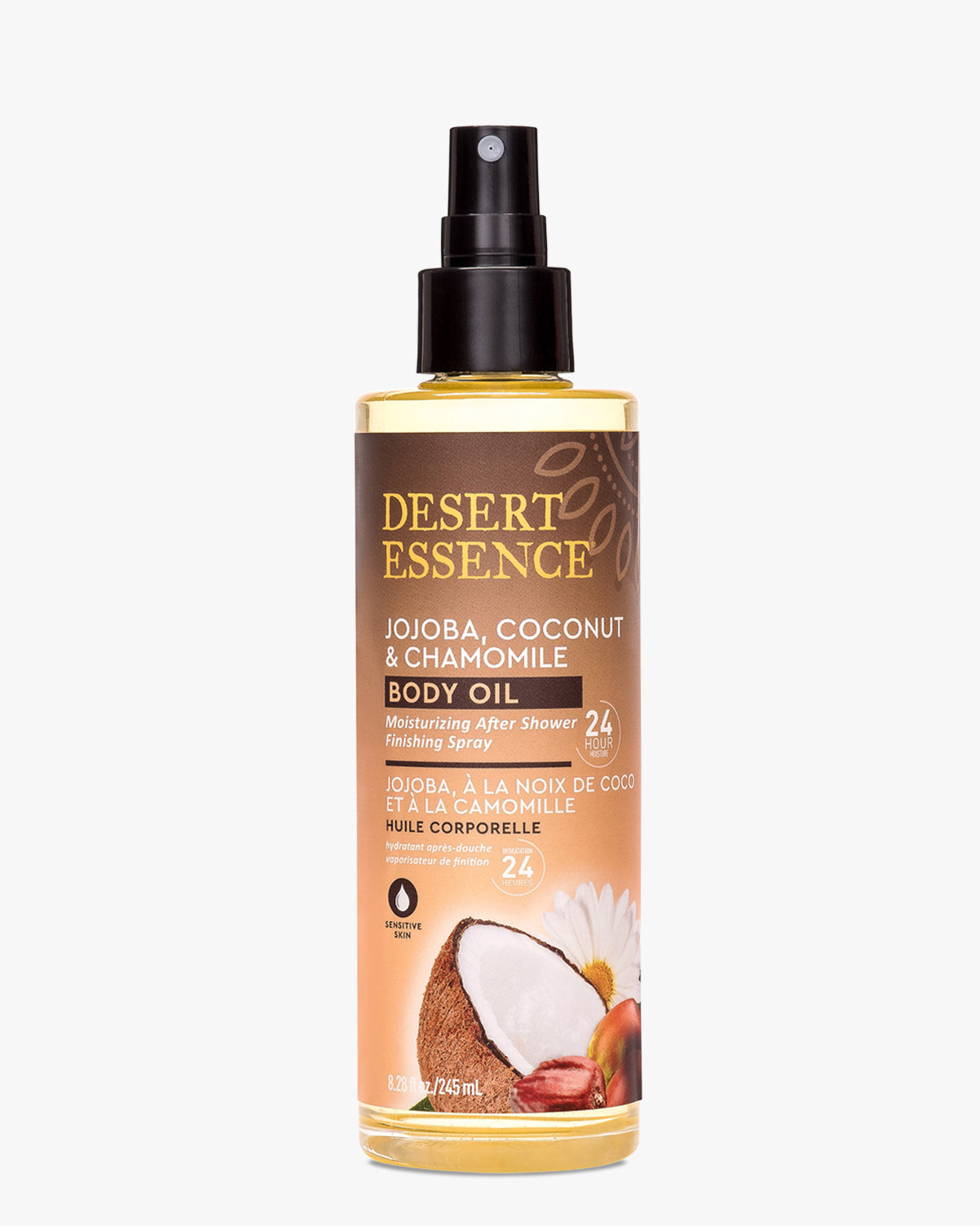 Desert Essence Jojoba, Coconut & Chamomile Body Oil Spray bottle featuring a gradient brown-to-peach label design with coconut and chamomile flower imagery. Clear glass bottle displays golden-hued oil with black spray pump dispenser.