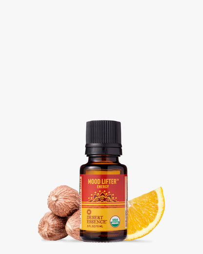 Mood Lifter Organic Essential Oil bottle displayed with fresh orange slice and whole nutmegs, featuring a warm red-orange label design against white background. The amber glass bottle shows USDA organic certification and Desert Essence branding.