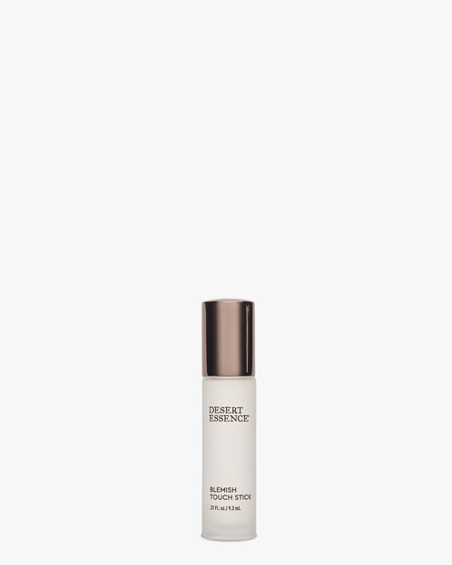 Desert Essence Blemish Touch Stick in a frosted glass bottle with metallic bronze cap, featuring a rollerball applicator for targeted treatment of skin imperfections. Natural skincare product against white background.