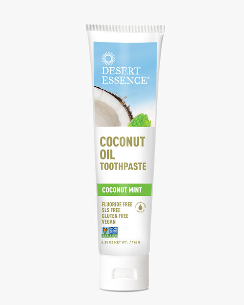 Desert Essence Coconut Oil Toothpaste tube in white packaging with blue sky and coconut imagery, featuring coconut mint flavor, fluoride-free formula in a natural oral care product against white background