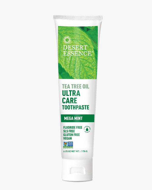 Desert Essence Tea Tree Oil Ultra Care Toothpaste tube featuring vibrant green leaf imagery, white packaging with green text, highlighting mega mint flavor and natural ingredients. Fluoride-free, SLS-free, and vegan-friendly oral care product.