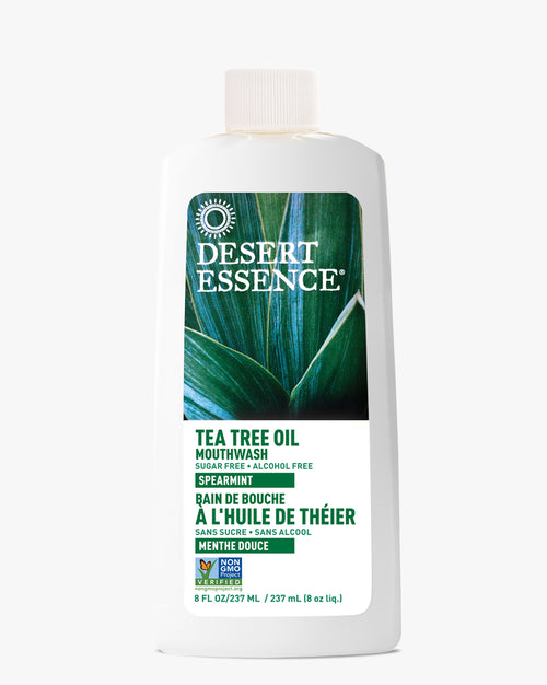 Desert Essence Tea Tree Oil Mouthwash with Spearmint, featuring a white bottle with green botanical design. Natural oral care product displaying sugar-free and alcohol-free labels, 8 oz size with bilingual text and Non-GMO certification.