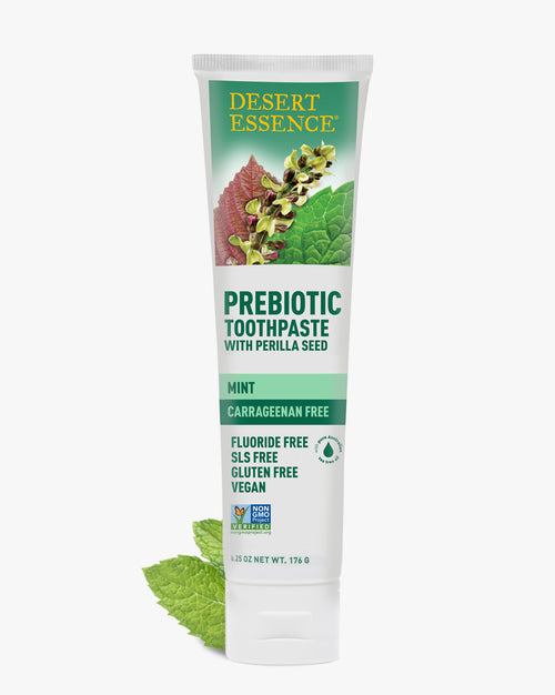 Desert Essence Prebiotic Mint Toothpaste tube with perilla seed, featuring a white and green design with botanical illustrations. Carrageenan-free, fluoride-free natural toothpaste with fresh mint leaves shown against a clean white background.