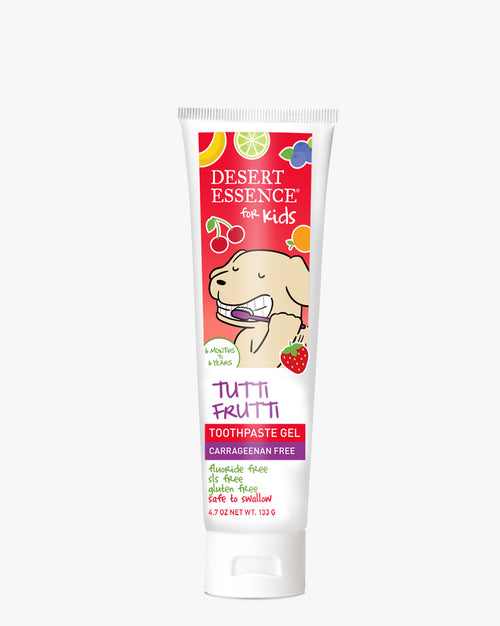 Tutti Frutti Gel Toothpaste for Kids featuring a cheerful cartoon dog brushing teeth on a vibrant red background with colorful fruit illustrations. White tube with Desert Essence branding and fruity design elements.